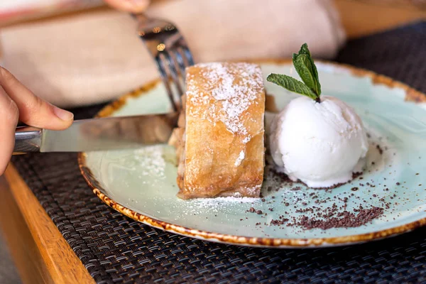 Strudel de maçã com sorvete de baunilha e hortelã. As mãos são cortadas com uma faca e garfo . — Fotografia de Stock