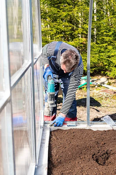 Construction of a garden greenhouse in the garden or vegetable garden. the Foundation and frame of beds with earth. The concept of healthy, home ecological nutrition. A man working with a drill.