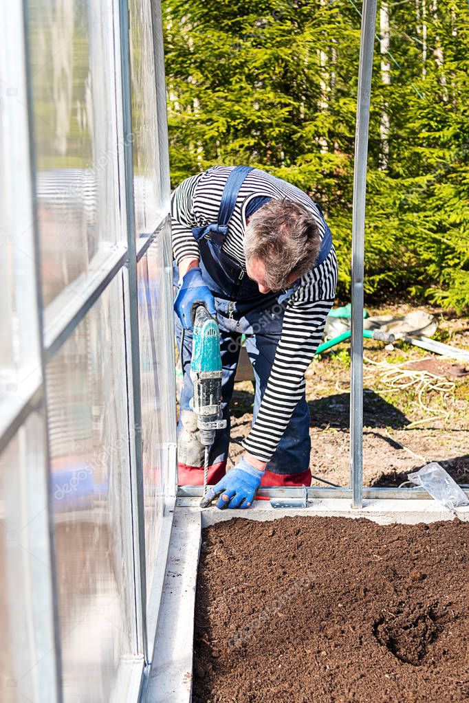 Construction of a garden greenhouse in the garden or vegetable garden. the Foundation and frame of beds with earth. The concept of healthy, home ecological nutrition. A man working with a drill.