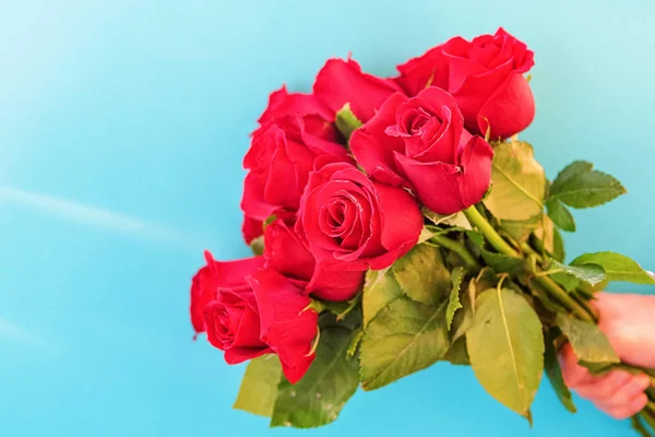 Muž má kytici krásných červených růží na modrém pozadí, zblízka. Mezinárodní den žen, narozeniny, den matek, Valentýn — Stock fotografie