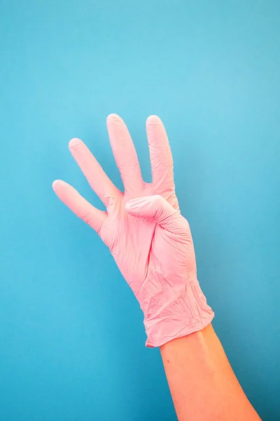 Apuntando con el dedo al número cuatro, usando guantes médicos rosados, sobre un fondo azul . — Foto de Stock