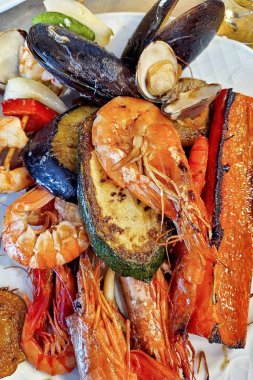 Yakın çekimde deniz ürünleri ve ızgara sebzeler içeren bir yemek. Karışık deniz ürünleri yemeği.