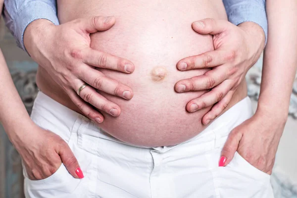 一张裸孕肚子的特写照片 男人的手紧紧抓住怀孕妻子的腹部 — 图库照片