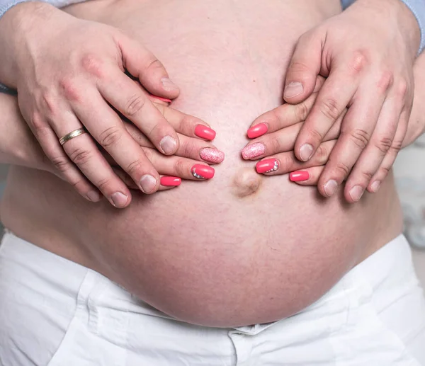一张裸孕肚子的特写照片 男人的手紧紧抓住怀孕妻子的腹部 — 图库照片