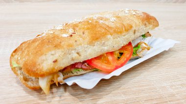 Ciabatta sandviçi, marul, tavuk ve peynirli ahşap bir masada.
