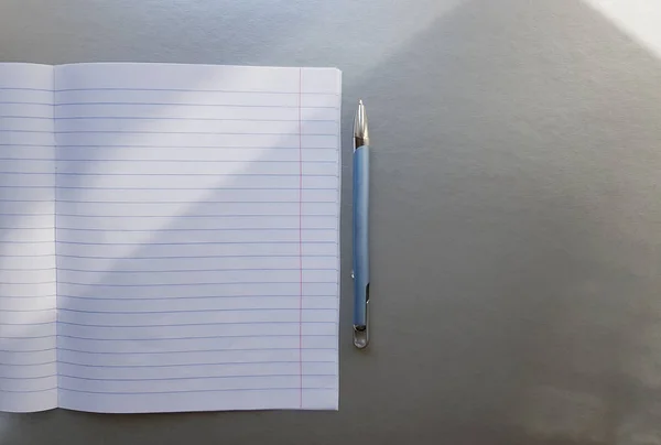 打开学校笔记本，用钢笔放在灰色的书桌上，窗户上有阳光。一张空白的白色笔记本，用于书写。教育理念。复制空间。从上面查看。平铺 — 图库照片