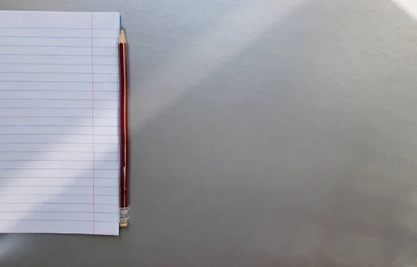Otevřený školní zápisník s perem na šedém stole se slunečními paprsky z okna. Prázdný bílý list poznámkového bloku pro psaní. vzdělávací koncept. Kopírovat místo pohled shora. Plochá ležela — Stock fotografie