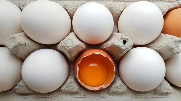 Ένα αυγό κοτόπουλου είναι μισοσπασμένο μεταξύ άλλων αυγών. Κοντινά πλάνα σε ένα δίσκο χαρτιού για αποθήκευση — Φωτογραφία Αρχείου