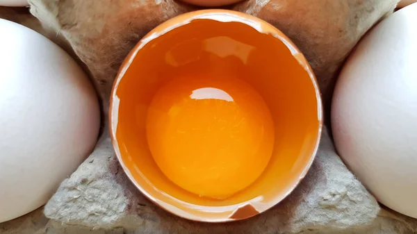 Ein Hühnerei ist halb zerbrochen unter anderen Eiern. Nahaufnahmen in einem Papierkorb zur Aufbewahrung — Stockfoto