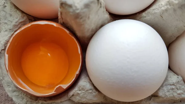Ένα αυγό κοτόπουλου είναι μισοσπασμένο μεταξύ άλλων αυγών. Κοντινά πλάνα σε ένα δίσκο χαρτιού για αποθήκευση — Φωτογραφία Αρχείου