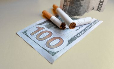 Klasik sigaralar 100 Amerikan doları banknotun üzerinde duruyor. Sarı bir arka plan üzerinde yüz dolarlık banknot sigara