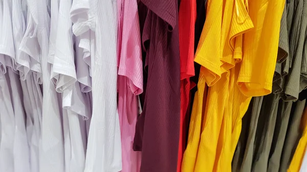 Kleuren van de regenboog. Verscheidenheid van casual shirts, t-shirts op hangers in een winkel. Doek katoen van verschillende felle kleuren close-up. Textiel achtergrond — Stockfoto