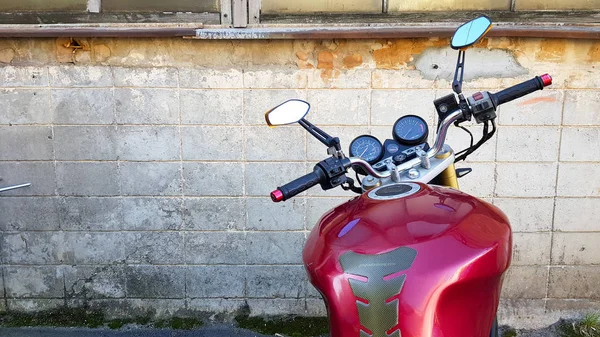 Czerwony motocykl zaparkowany w szarej ścianie cegły. Widok pierwszoosobowy, deska rozdzielcza i kierownica — Zdjęcie stockowe