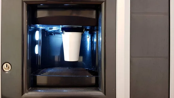 Coupe en papier blanc dans la fenêtre d'une machine à café distributrice. Le processus de fabrication du café dans une machine à laver — Photo