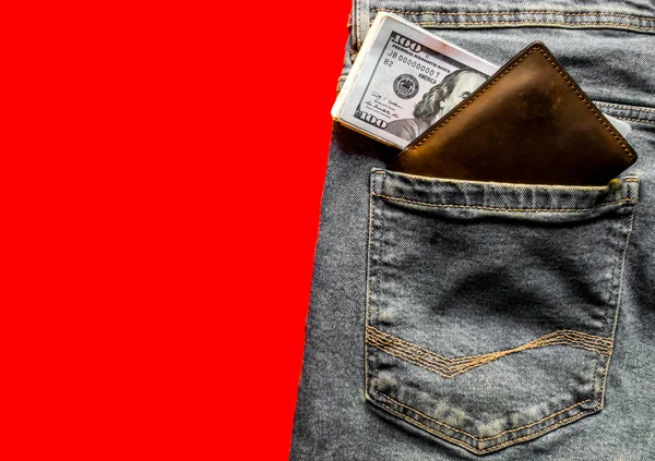banknotes in your jeans pocket in your wallet. The concept of wealth and wages for work. Wallet and dollars in jeans pocket. Copy space, place for text, flat lay. Blue jeans on a red background