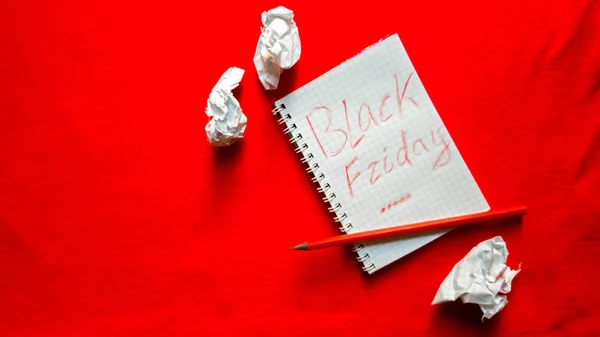 Black friday sale text written on a notepad with a red pencil on a red background. Background, holiday concept. Black Friday - International Day of Shopping, Promotions, Discounts, Sales. Sales season