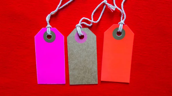 Trois étiquettes colorées sur une corde blanche, fond rouge — Photo