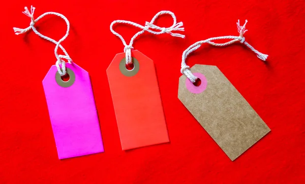 Trois étiquettes colorées sur une corde blanche, fond rouge — Photo