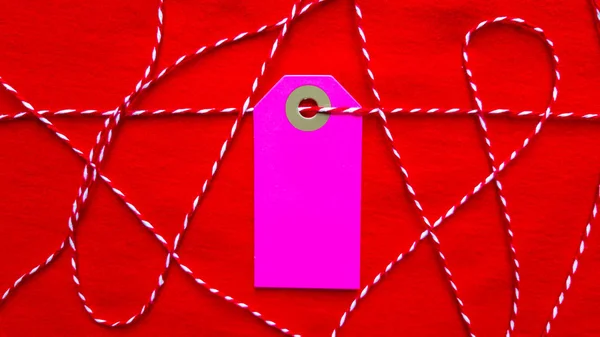 Une étiquette violette sur une corde rouge repose sur un fond rouge. Espace de copie, place pour le texte, pose plate . — Photo