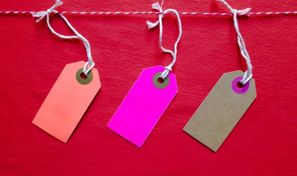 Trois étiquettes lumineuses colorées pendent sur une corde rouge sur un fond rouge. Espace de copie, place pour le texte, pose plate . — Photo