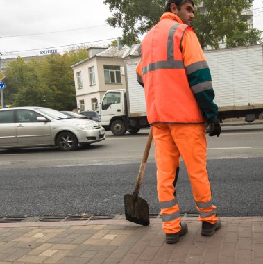 Ukrayna, Kiev - 22 Eylül 2019: Turuncu üniformalı işçiler bir şehir caddesinde asfalt döşeyenler. Yol makineleri. Şehir ekonomisi. İşçi adam asfalt yol koyar, kaldırım yol onarım