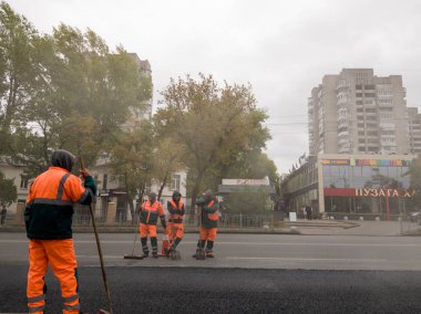 Ukrayna, Kiev - 22 Eylül 2019: Turuncu üniformalı işçiler bir şehir caddesinde asfalt döşeyenler. Yol makineleri. Şehir ekonomisi. İşçi adam asfalt yol koyar, kaldırım yol onarım