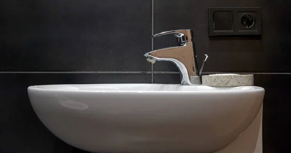 Salle de bain intérieure avec lavabo et robinet. Appartement moderne dans le grenier de la maison. Lavabo en céramique blanche avec robinet chromé sur un mur de tuiles noires — Photo