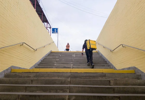 Украина, Киев - 26 сентября 2019 года: Гуляющий курьер Глово с желтым рюкзаком поднимает ступени перехода, спешит доставить заказ вовремя заказчику — стоковое фото