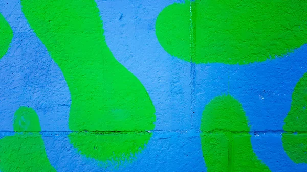 De betonnen muur is geschilderd in groene en blauwe camouflage. Vlekken van verf op een stenen muur, kleurrijke achtergrond met Kopieer ruimte. — Stockfoto