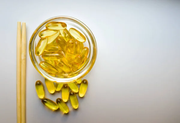 Fish oil capsules on a saucer with chopsticks. Capsules of fish oil. Omega 3 fish oil capsules on white background. Pile of capsules Omega 3 on white background. Close up, top view, high resolution