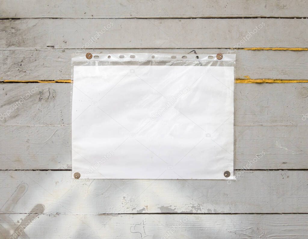 White paper sign with rivets, vintage background on a gray wooden old backdrop. Wooden textured wall, weighs a white blank cardboard sign lit by the sun, closeup