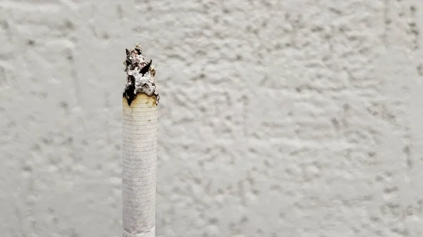 Koncept pasivního kouření. V den bez tabáku je kouření pro společnost nežádoucí. Vertikální cigareta kouřící na bílém pozadí stěny s kopírovacím prostorem. Text ne cigaretám. — Stock fotografie