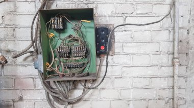 Evin duvarındaki eski elektrik paneli. Eski evin beyaz tuğla duvarındaki elektrik panelinden elektrik kabloları sarkıyor..