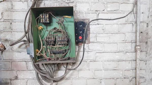 Evin duvarındaki eski elektrik paneli. Eski evin beyaz tuğla duvarındaki elektrik panelinden elektrik kabloları sarkıyor..