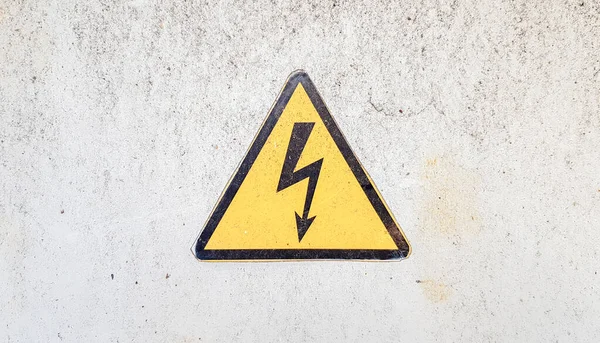 Fara tecken på högspänning el. Gul triangulär skylt med en blixt i mitten. Denna varning är skriven på en gammal metallyta målad med grå färg. — Stockfoto