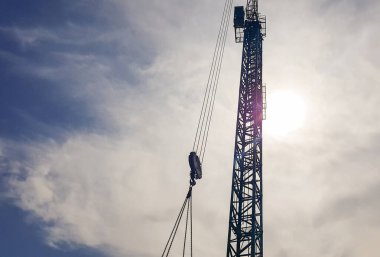 Mavi gökyüzünün arka planında inşaat vinci. İnşaat vincinin yakın görüntüsü. Gökyüzünde bulutlu bir vinç silueti olan soyut endüstriyel bir arka plan..
