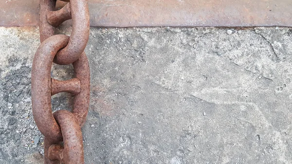 Rusty iron chain on concrete. Chain anchors are buried in concrete for mooring in the port. Background with copy space. Thick, massive, rusty chains on a concrete-rocky surface