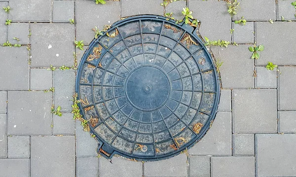 Plastic manhole cover, round edge. One old black plastic trash plastic cap on a cement floor. Cast iron manhole on paved road, manhole cover — Stock Photo, Image