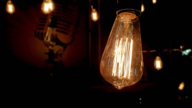 Işık dekoru. Eskimiş bir arka planda asılı bir Edison ampulü. Karanlıkta parlayan eski tozlu ampuller. Dekoratif cam lambanın içinde bir lamba. Işık ortaya çıkmaya ve ortada parlamaya başlar..