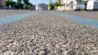 Asfalt-siyah bir yüzeyde geniş mavi bir şerit. Şehirde asfalt yol, yaz, yeşil ağaçlar, mavi gökyüzü. Orta mavi çizgilerden düşük açı görünümü.