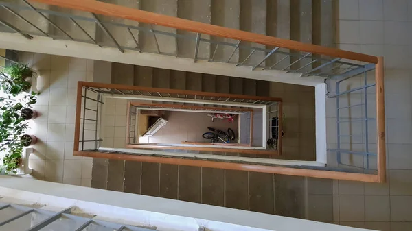 Konut binasındaki modern merdiven boşluğu. Merdiven perspektifi. Gri seramik fayans. Kahverengi ahşap çitli ve beton basamaklı ortak merdivenler. Yukarıdan görüntüle
