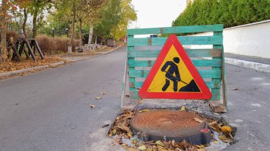 Yol tamiri. Yolda kanalizasyon boşluğu var. Üçgen uyarı otomobil sürücüleri sarı kürekli ve kırmızı atlı bir adamla anlaşma imzalarlar. İş yerindeki erkekler. Trafik işaretleri, seyahat kısıtlamaları