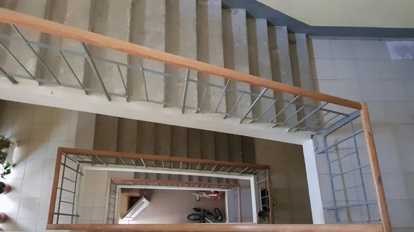 Konut binasındaki modern merdiven boşluğu. Merdiven perspektifi. Gri seramik fayans. Kahverengi ahşap çitli ve beton basamaklı ortak merdivenler. Yukarıdan görüntüle