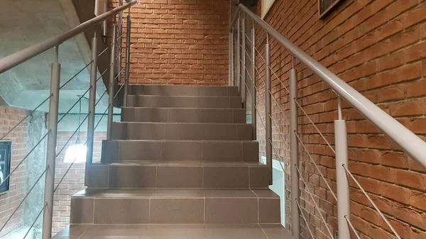 Red brick building with a modern staircase in a loft style with metal railing. Stairs adorn the building. Modern stairwell. Steel railing. Staircase in perspective