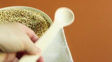 Tabakta pişmemiş organik yeşil karabuğday. Ahşap kaşıklı bir kadın eli homurdanmaları ayırıyor veya topluyor