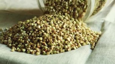 Yeşil çiğ karabuğday masadaki cam kavanozdan yavaşça dökülür. Karabuğday, video 4k 'yi çekiyor. Tarım. Sağlıklı ve vejetaryen yemekleri masada. Evde yemek pişir. Güvenli, ekolojik ve sağlıklı ürün.