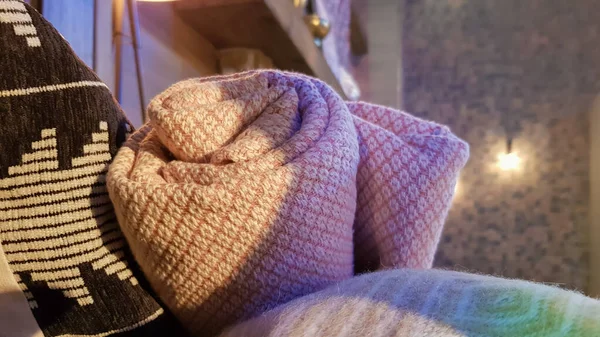 Knitted and warm blankets are folded and laid in a wicker basket near the fireplace. Cozy interior in the house. Details of a modern cozy interior.