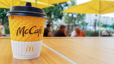 McDonalds restoranında McCafe menüsü. Açık bir masada sarı bir fincan kahve, sarı şemsiyeler ve arka planda ziyaretçiler. Kahvaltı, kahve zamanı. Ukrayna, Kiev - 6 Eylül 2019