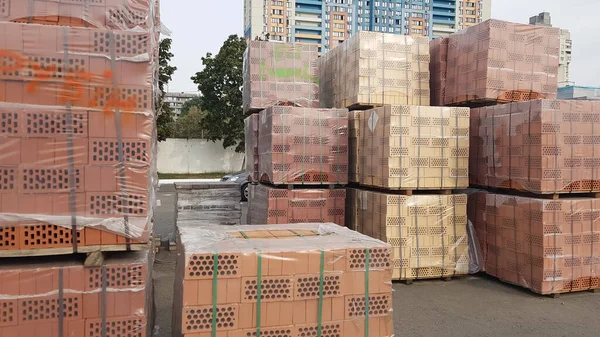 Red perforated bricks with rectangular holes on wooden pallets in an open-air warehouse ready for sale. New bricks on pallets at a hardware store