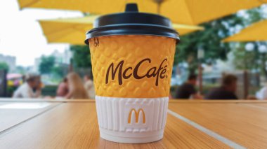 McDonalds restoranında McCafe menüsü. Açık bir masada sarı bir fincan kahve, sarı şemsiyeler ve arka planda ziyaretçiler. Kahvaltı, kahve zamanı. Ukrayna, Kiev - 6 Eylül 2019